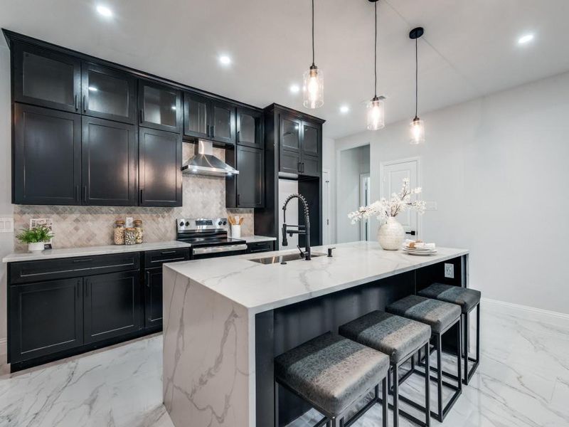 Kitchen with dark cabinetry, light marble finish flooring, light stone countertops, a breakfast bar, and decorative backsplash.