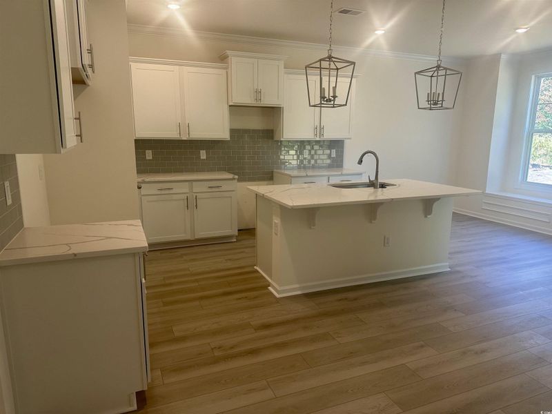 Kitchen featuring tasteful backsplash, quartz  countertops, white cabinetry, a kitchen breakfast bar, and crown molding