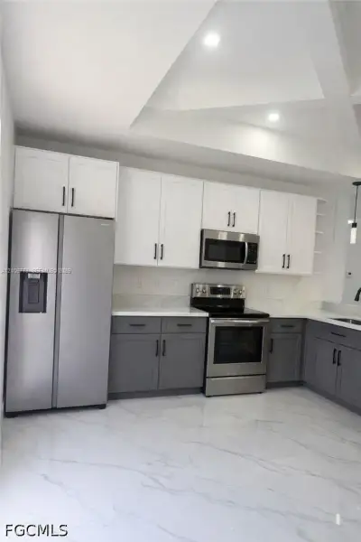Kitchen featuring two-tone cabinetry, stainless steel appliances, stone-finish countertops, tile flooring, and tray ceiling with recessed lighting Kitchen featuring two-tone cabinetry, stainless steel appliances, stone-finish countertops, tile flooring, and tray ceiling with recessed lighting