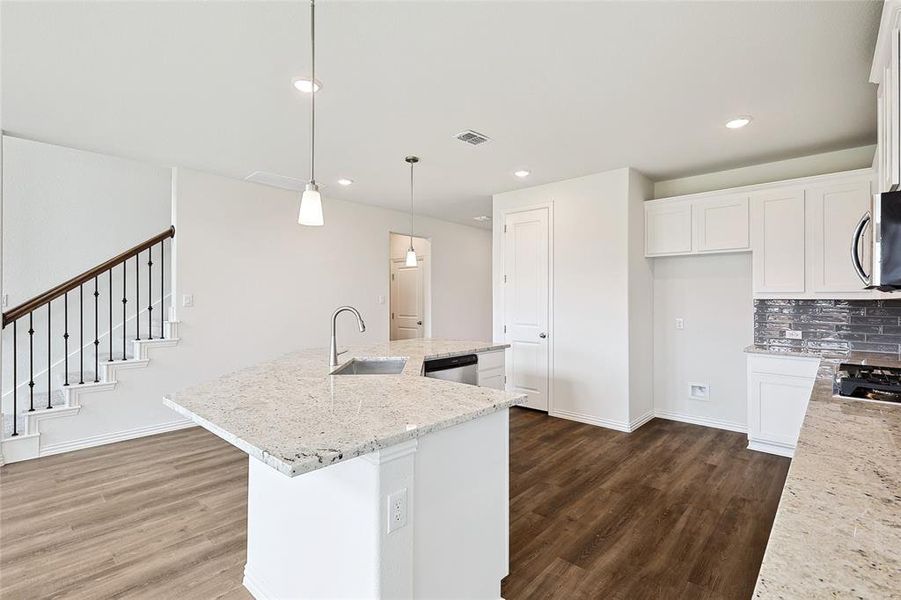 Kitchen featuring decorative light fixtures, light stone countertops, a center island with sink, and sink