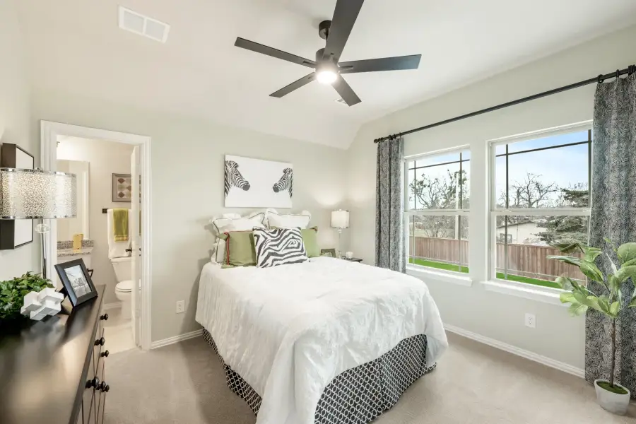 Bedroom with vaulted ceiling, ceiling fan, ensuite bathroom, and two large windows with backyard view