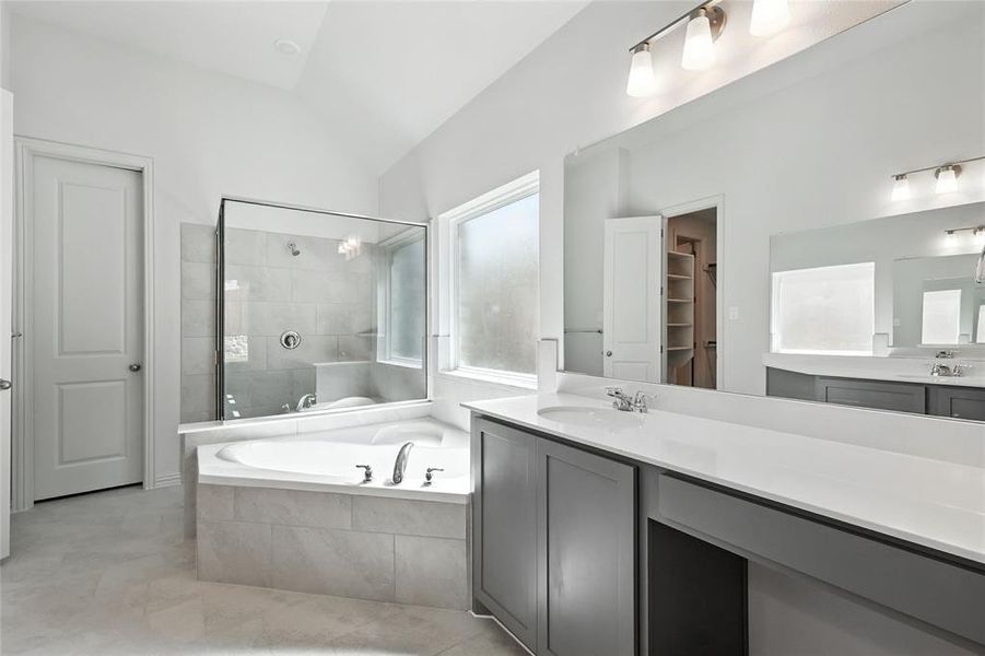Bathroom featuring a bath, vaulted ceiling, vanity, tiled shower, and a walk in closet Bathroom featuring a bath, vaulted ceiling, vanity, tiled shower, and a walk in closet