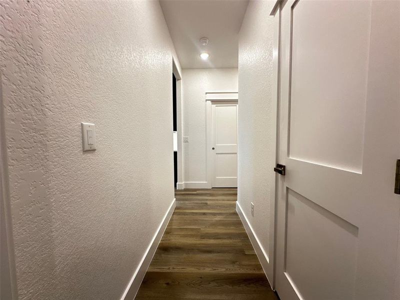 Hallway featuring baseboards, a textured wall, dark wood-style floors, and recessed lighting
