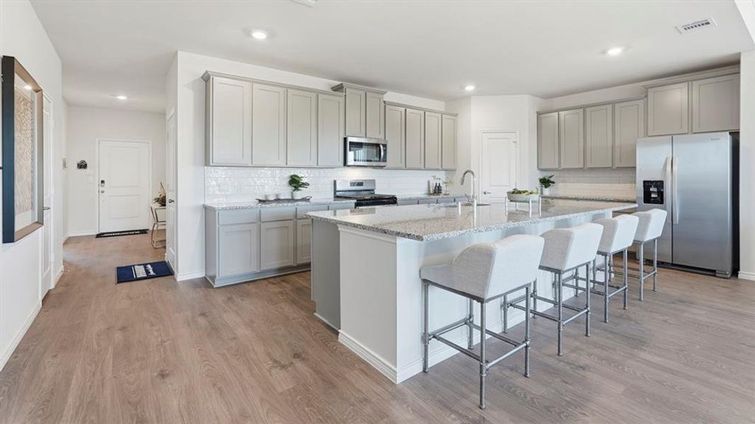 Kitchen featuring gray cabinets, stainless steel appliances, light stone countertops, a breakfast bar area, and a kitchen island with sink