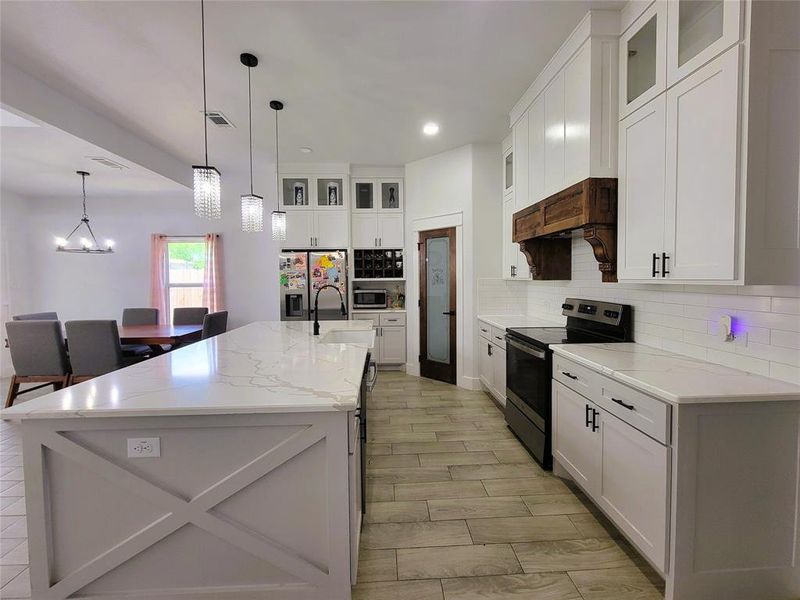 Kitchen featuring glass fronted cabinets, stainless steel appliances, white cabinets, a kitchen island with sink, and light stone counters