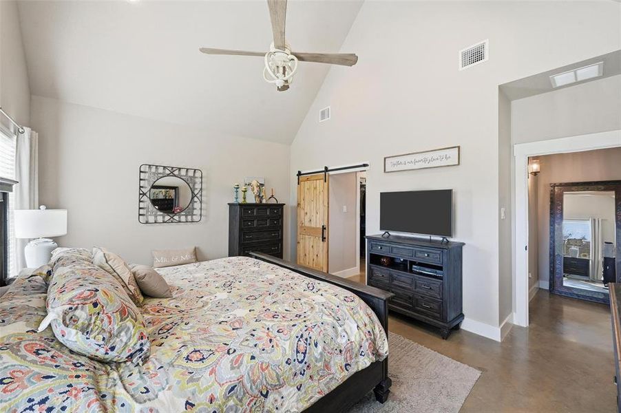 Bedroom featuring a barn door, high vaulted ceiling, finished concrete flooring, and ceiling fan Bedroom featuring a barn door, high vaulted ceiling, finished concrete flooring, and ceiling fan