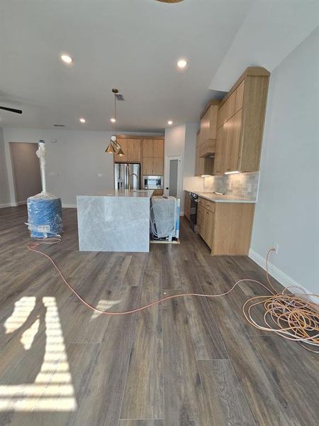 Kitchen featuring hanging light fixtures, dark wood finished floors, an island with sink, modern cabinets, and decorative backsplash