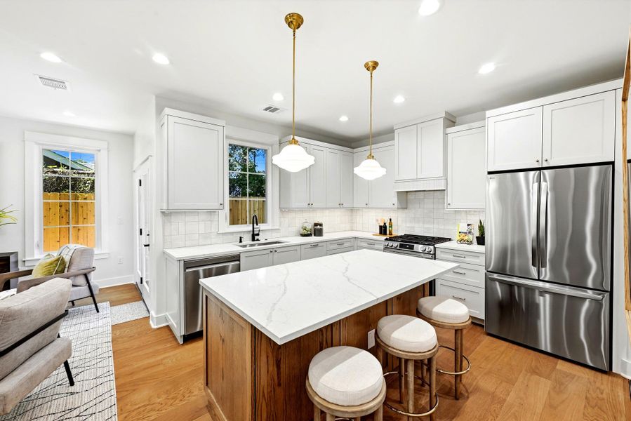 A contemporary kitchen features bright white cabinetry, stainless steel appliances, a generous island with seating, and warm hardwood flooring. A contemporary kitchen features bright white cabinetry, stainless steel appliances, a generous island with seating, and warm hardwood flooring.