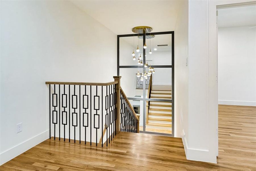 Stairwell featuring custom metal balusters, natural wood handrail, and wood-finish flooring Stairwell featuring custom metal balusters, natural wood handrail, and wood-finish flooring