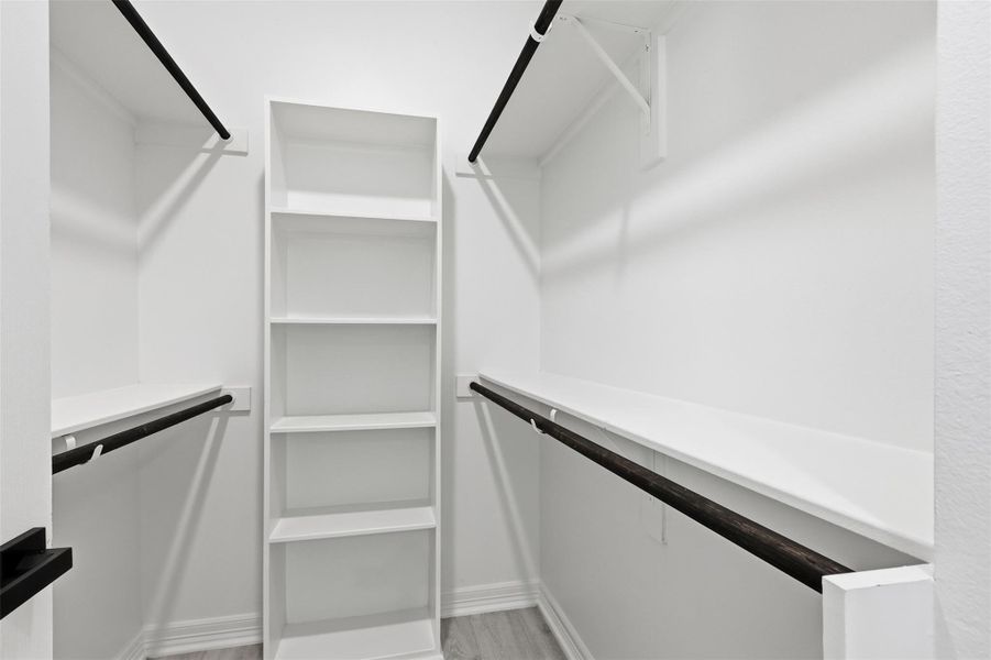 Large walk in closet featuring custom built in white shelving system with multiple rods and storage levels.