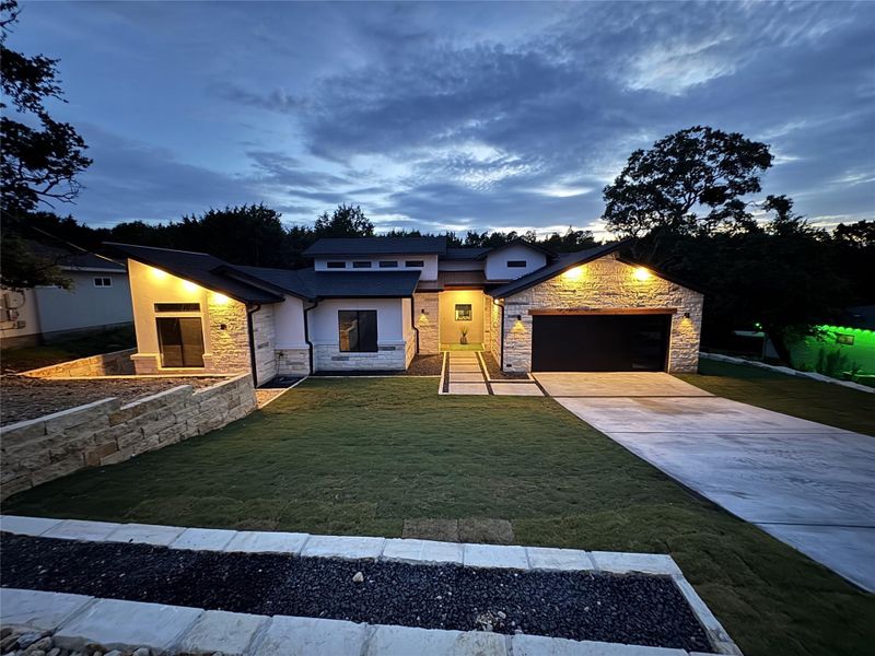 Contemporary home featuring an attached garage, concrete driveway, stone siding, and a front lawn Contemporary home featuring an attached garage, concrete driveway, stone siding, and a front lawn