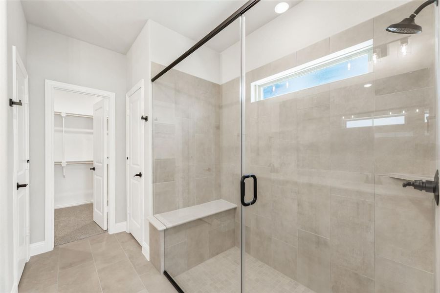 Walk-in shower with glass door, tile walls, built-in bench, and rain showerhead, with walk-in closet visible in background