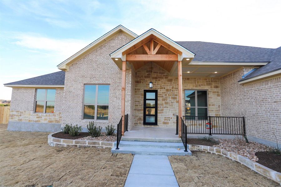 Entrance to property with covered porch, a shingled roof, stone siding, and brick siding