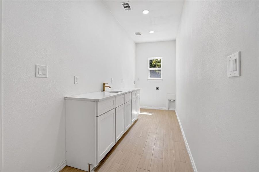 Utility room featuring wood-finish flooring, white cabinetry, a light-toned countertop, and a window for natural light