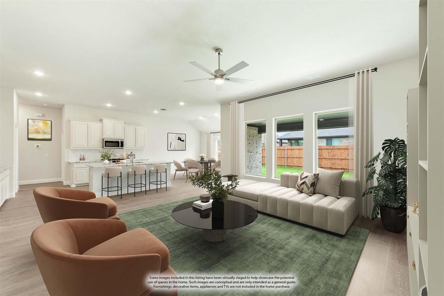 Open-concept living room with ceiling fan, hardwood floors, and kitchen with white cabinets visible in background Open-concept living room with ceiling fan, hardwood floors, and kitchen with white cabinets visible in background