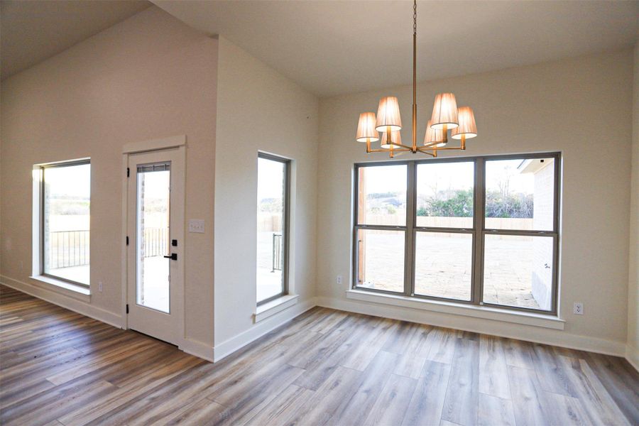 Unfurnished dining area featuring a chandelier, light wood-style floors, vaulted ceiling, and plenty of natural light