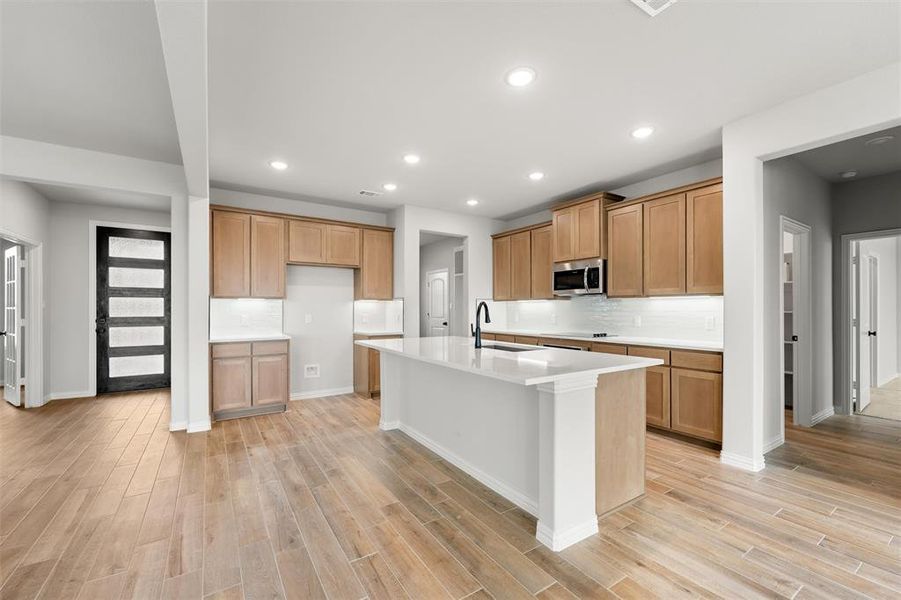 Kitchen with recessed lighting, stainless steel microwave, an island with sink, light wood-type flooring, and backsplash Kitchen with recessed lighting, stainless steel microwave, an island with sink, light wood-type flooring, and backsplash