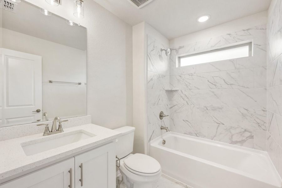 Bathroom with white vanity, quartz countertop, and marble-tiled tub and shower combo