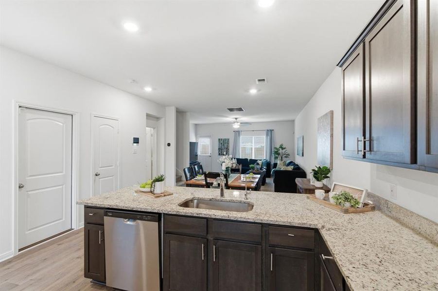 The kitchen features a stainless steel dishwasher, a sink with a gooseneck faucet, dark wood cabinetry, and light-colored granite countertops