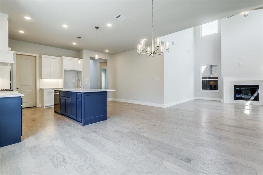 Kitchen with blue cabinets, light wood-type flooring, a kitchen island with sink, white cabinetry, and hanging light fixtures