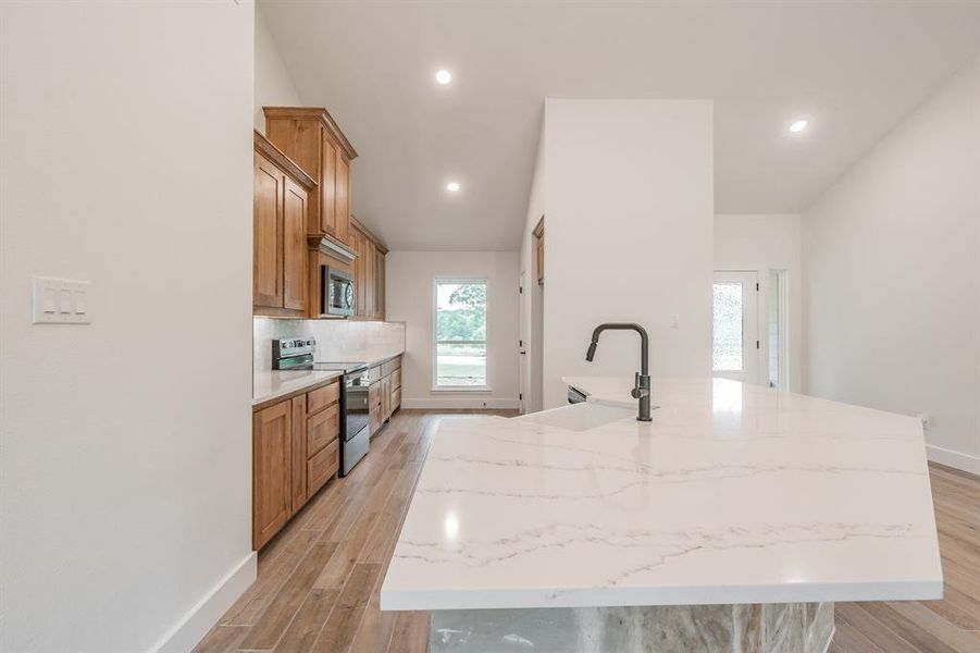 Kitchen featuring appliances with stainless steel finishes, a sink, a spacious island, baseboards, and brown cabinetry
