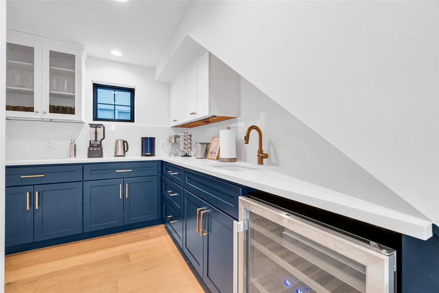 Kitchen with blue cabinetry, white cabinets, glass insert cabinets, wine cooler, and light wood-style flooring Kitchen with blue cabinetry, white cabinets, glass insert cabinets, wine cooler, and light wood-style flooring