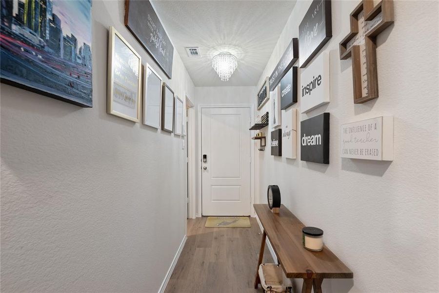 Doorway to outside with wood finished floors, a chandelier, and a textured wall