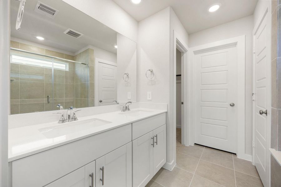 The primary bath features a sleek dual vanity, modern fixtures, and a spacious glass-enclosed shower. Clean lines and bright finishes create a refreshing, spa-like atmosphere designed for everyday comfort and relaxation.
