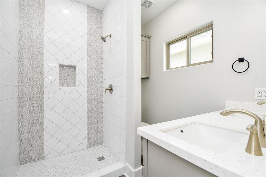 This is a modern Master  bathroom featuring a walk-in shower with decorative tile work, a single vanity with ample counter space, and a sleek design.