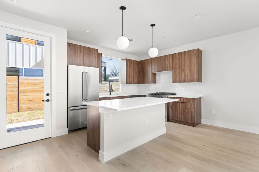 Kitchen featuring a kitchen island, light wood-style flooring, decorative backsplash, light countertops, and appliances with stainless steel finishes