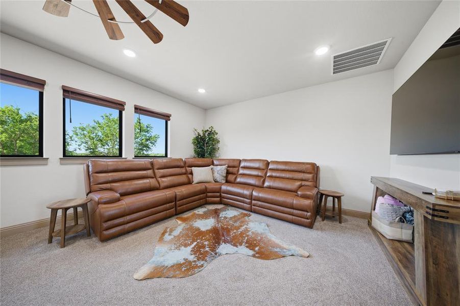 Carpeted room featuring three rectangular windows with dark frames and wood-finish blinds, a ceiling fan with wood-finish blades, recessed lighting, and a built-in wood-finish media console