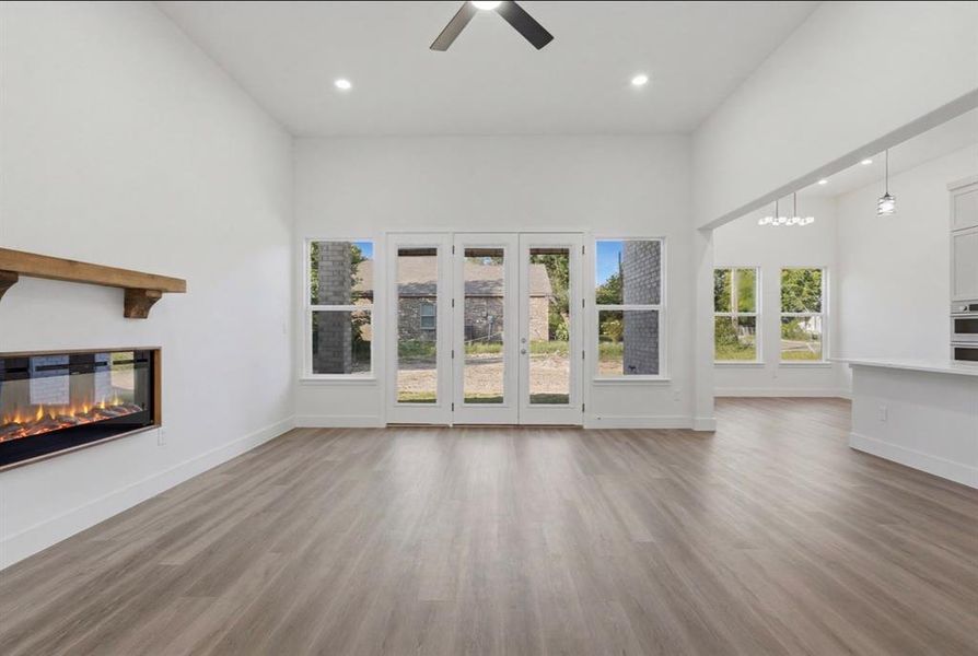 Spacious living area featuring wood-finish flooring, a contemporary electric fireplace with a rustic wood mantle, and a ceiling fan