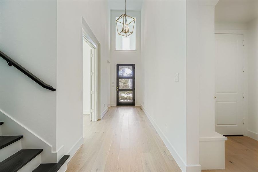 Foyer with light wood-style floors, stairs, a high ceiling, and a chandelier Foyer with light wood-style floors, stairs, a high ceiling, and a chandelier