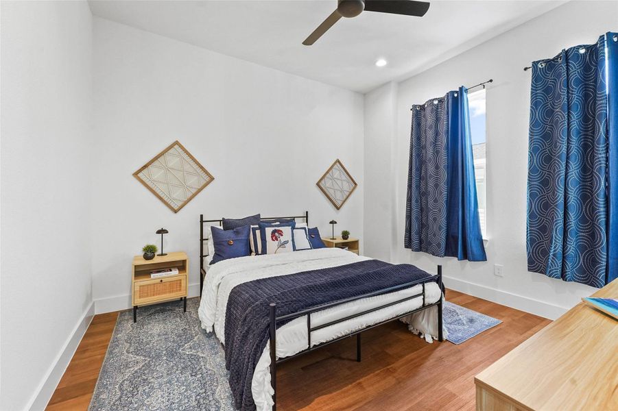 Bright and spacious bedroom featuring wood flooring, large windows with stylish curtains, and a modern ceiling fan. Bright and spacious bedroom featuring wood flooring, large windows with stylish curtains, and a modern ceiling fan.