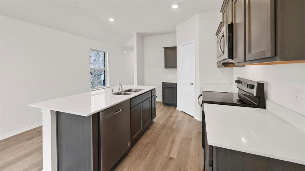 Kitchen with stainless steel appliances, a center island with sink, recessed lighting, light stone countertops, and light wood finished floors