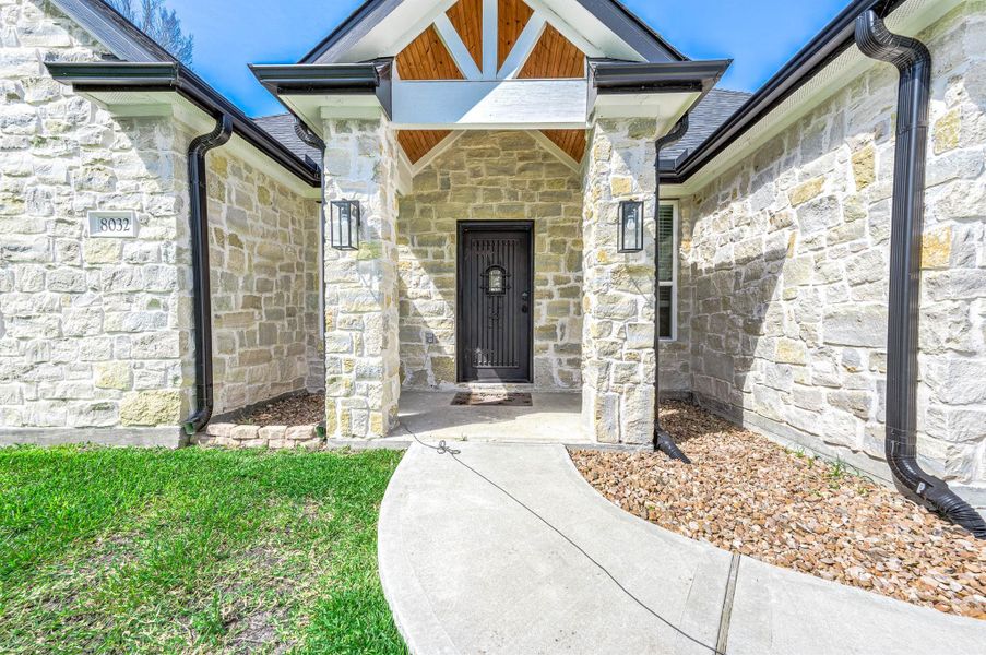 The front entry welcomes you with elegant stonework, a covered porch, and stylish modern lighting. Thoughtful landscaping and the arched walkway create a warm and inviting first impression