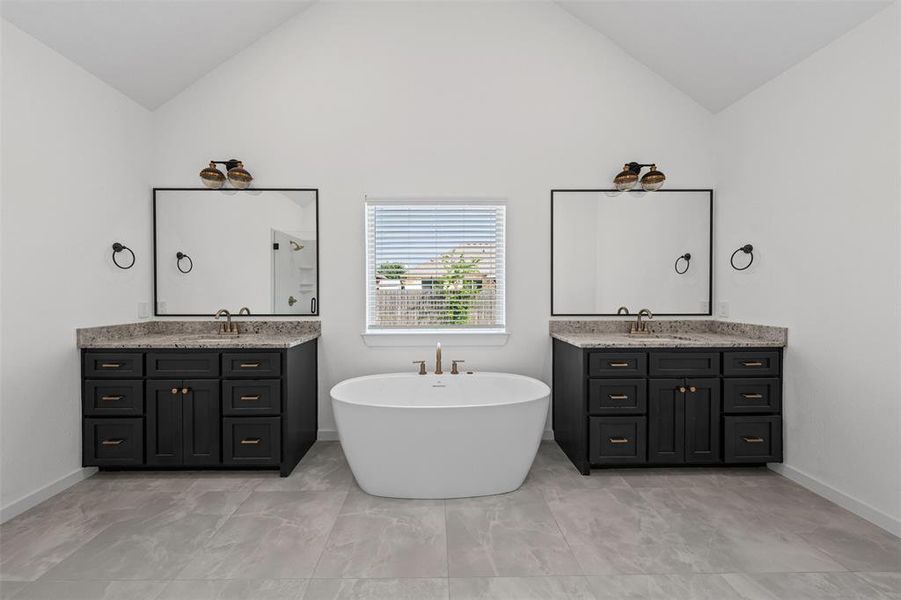 This bathroom features a vaulted ceiling, a freestanding soaking tub, and two vanity units with dark cabinetry and light-colored countertops