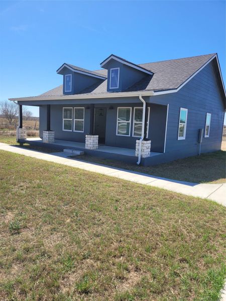 View of front of property with covered porch, a front lawn, and a shingled roof
