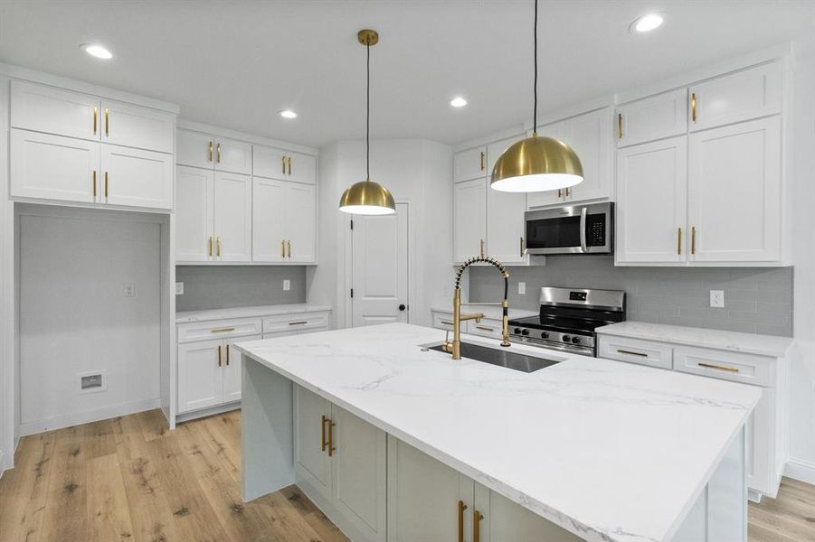 Kitchen with white cabinets, a kitchen island with sink, stainless steel appliances, light wood-style floors, and a sink