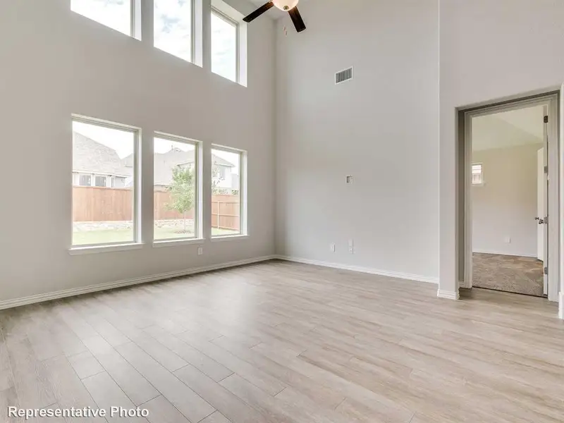 This room features high ceilings with a ceiling fan, light-toned plank flooring, and abundant natural light from multiple windows