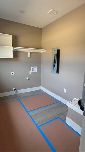 Washroom with electric dryer hookup, electric panel, baseboards, hookup for a washing machine, and wood finished floors Washroom with electric dryer hookup, electric panel, baseboards, hookup for a washing machine, and wood finished floors