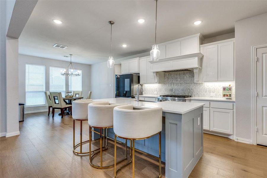 Kitchen with black refrigerator, white cabinets, light hardwood / wood-style flooring, and an island with sink