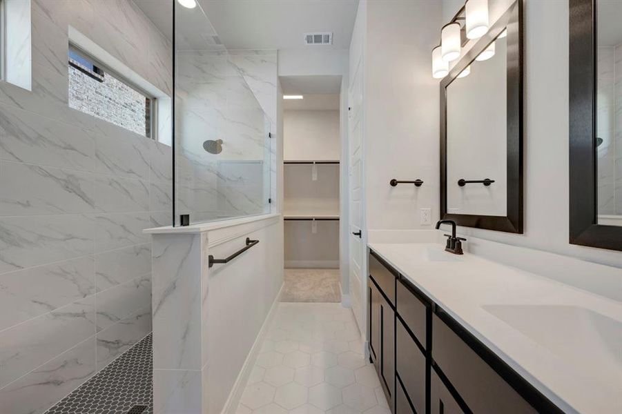 Full bath featuring a walk in closet, double vanity, a marble finish shower, and light tile patterned floors