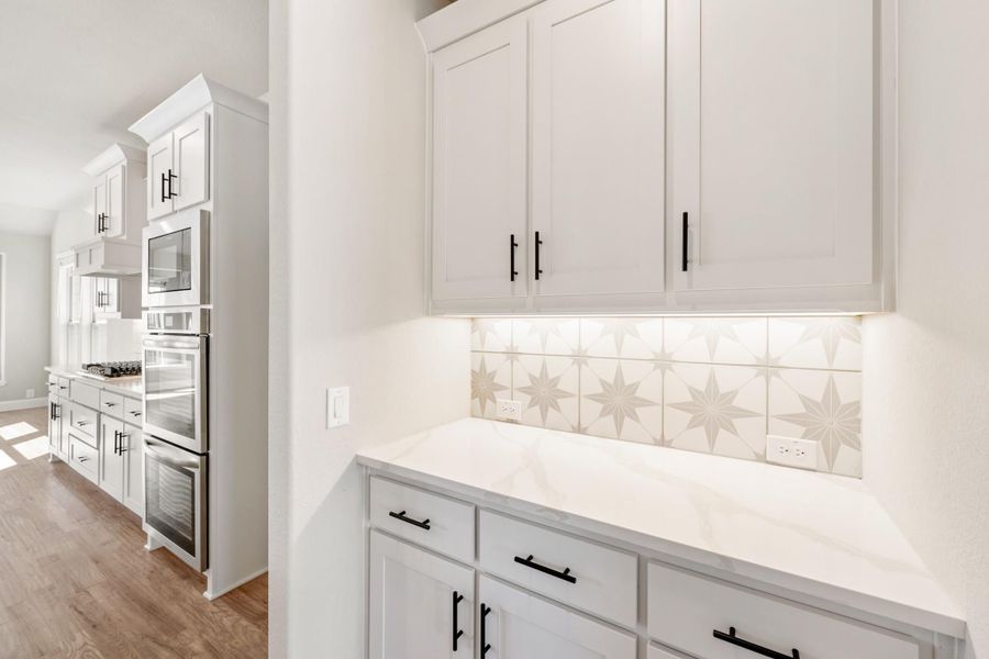 Kitchen with white cabinets, quartz countertop, star-pattern tile backsplash, and stainless steel double ovens