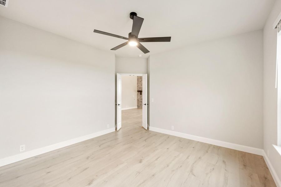 Empty bedroom with light wood floors, white walls, ceiling fan, and open doorway to hallway