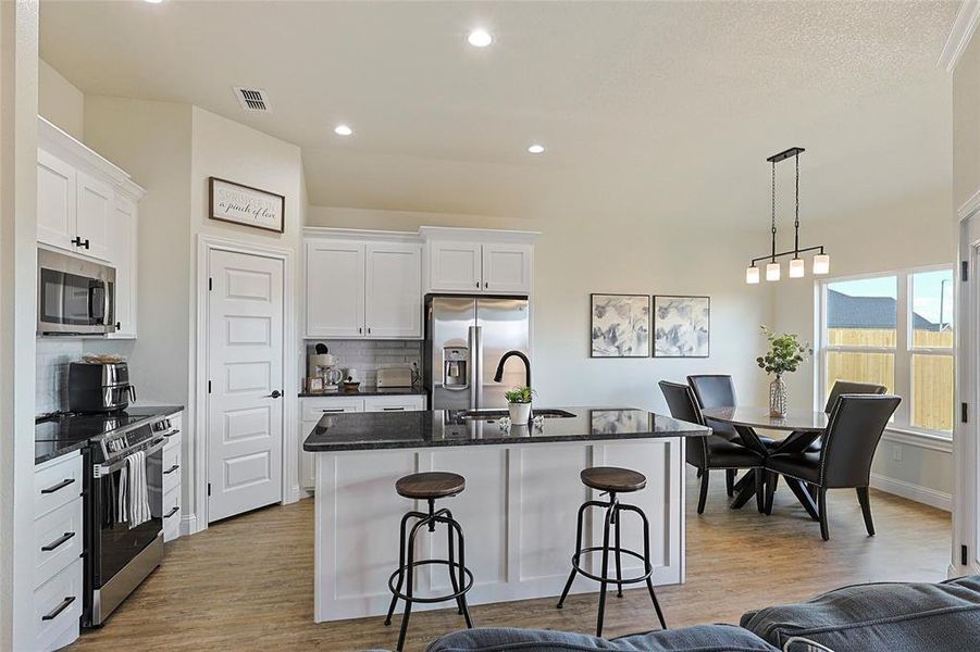 Open-concept kitchen featuring white shaker-style cabinetry, dark stone countertops, stainless steel appliances, and a central island with bar seating Open-concept kitchen featuring white shaker-style cabinetry, dark stone countertops, stainless steel appliances, and a central island with bar seating