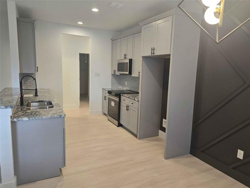 Kitchen featuring sink, decorative backsplash, custom granite countertops, light laminate floors, and stainless steel range oven