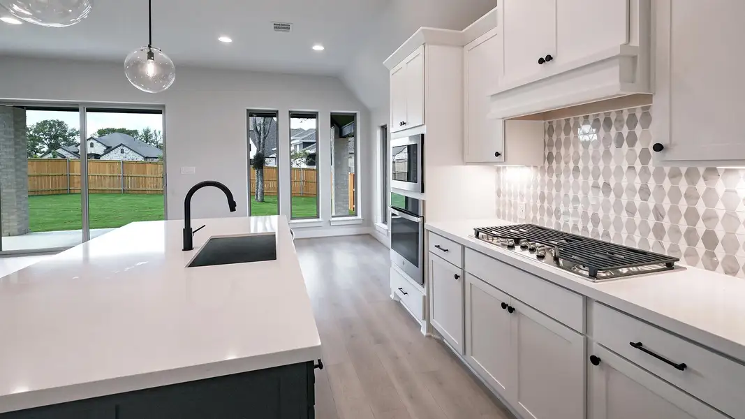 Kitchen with pendant lighting, white cabinetry, light wood finished floors, a kitchen island with sink, and appliances with stainless steel finishes