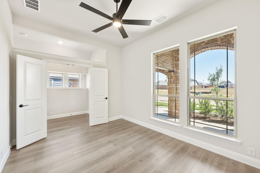 Empty bedroom with hardwood floors, ceiling fan, and large windows overlooking a stone porch exterior Empty bedroom with hardwood floors, ceiling fan, and large windows overlooking a stone porch exterior