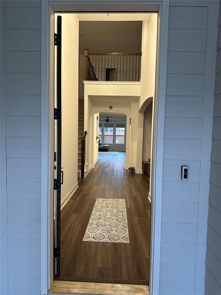 Entryway featuring wood-finish flooring, two-story foyer, iron and wood baluster railing, white trim, and an arched doorway Entryway featuring wood-finish flooring, two-story foyer, iron and wood baluster railing, white trim, and an arched doorway